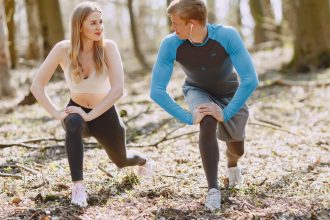 A couple engages in outdoor stretching exercises in a sunlit forest setting, promoting wellness and fitness.