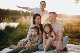 A family of five enjoying a serene picnic in a sunlit meadow during sunset.